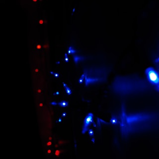 A string of bright blue LED lights arranged in a pattern, with smaller red lights forming a line to the left. The scene is dark, emphasizing the vivid glow of the lights against the shadowy background.
