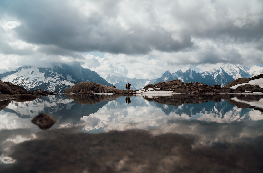 brown mountain near body of water under white clouds and blue sky during daytime