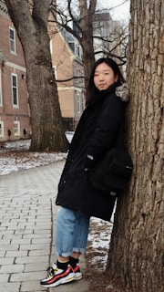 woman in black jacket standing beside brown tree during daytime