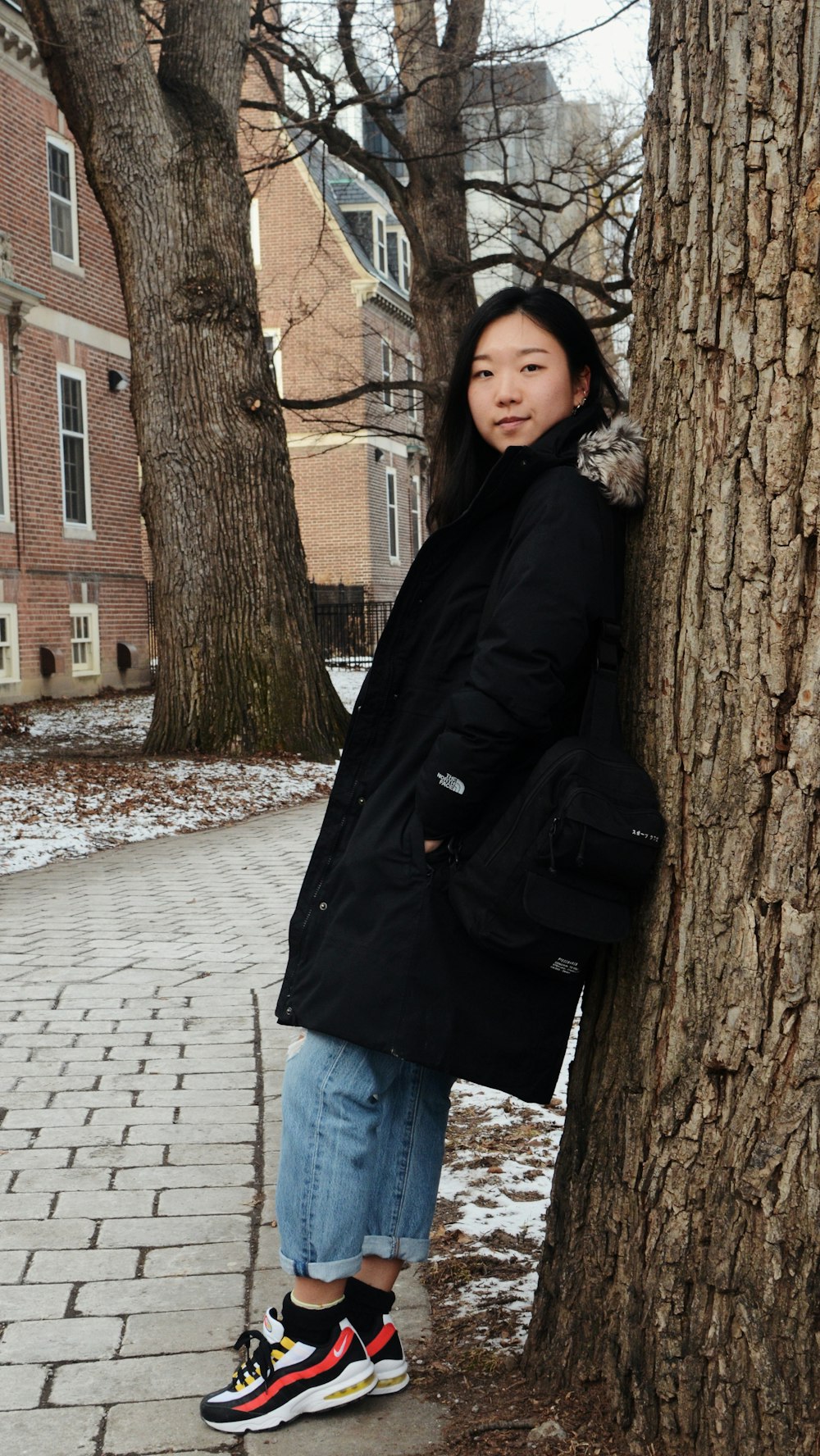 woman in black jacket standing beside brown tree during daytime