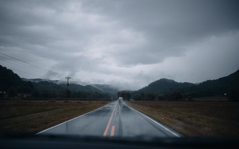 gray asphalt road between green grass field under gray cloudy sky during daytime