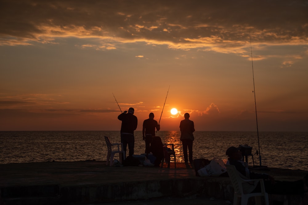 silhouette of people standing on beach during sunset