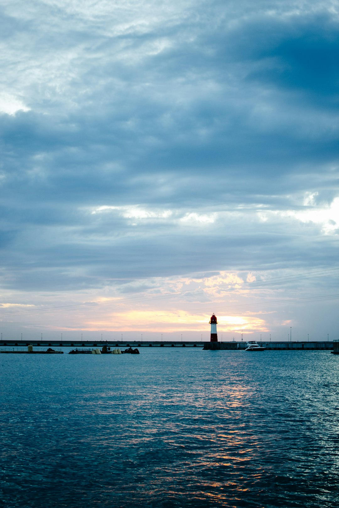 silhouette of lighthouse on sea dock under cloudy sky during daytime