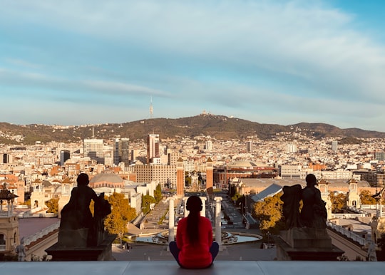 couple sitting on the edge of a building looking at the city during daytime in Plaça d'Espanya Spain
