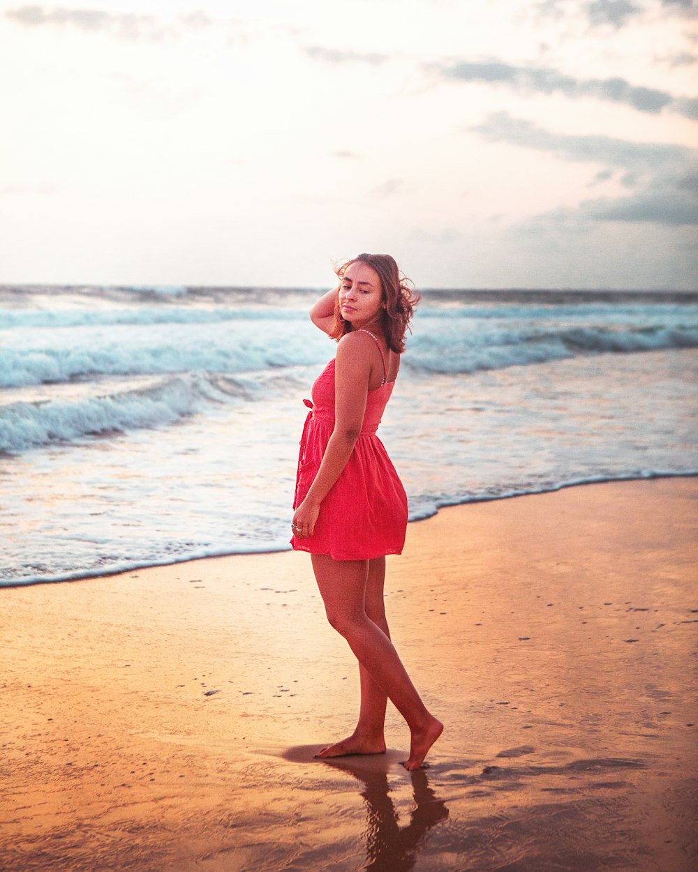 femme en robe rose debout sur la plage pendant la journée