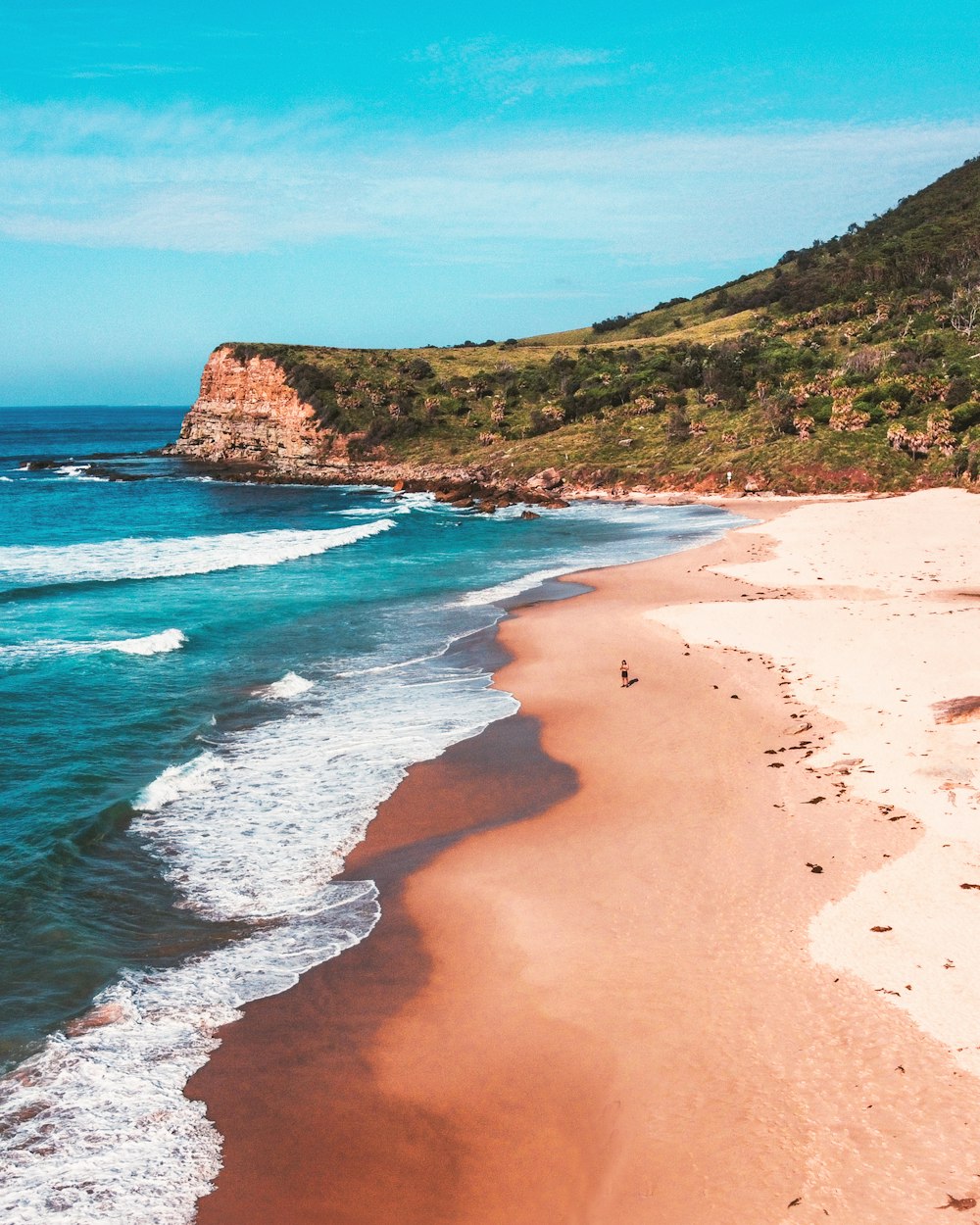 brown sand beach with green grass and brown mountain in distance