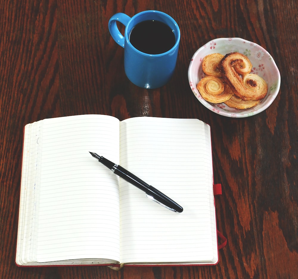 red ceramic mug beside black click pen on white paper