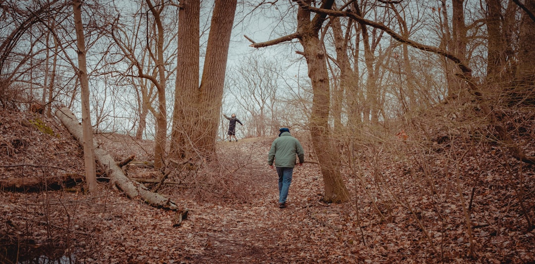 man in gray jacket and blue denim jeans standing near brown bare trees during daytime
