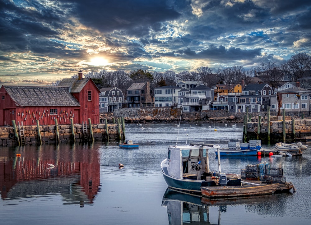 white and blue boat on body of water near houses under cloudy sky during daytime