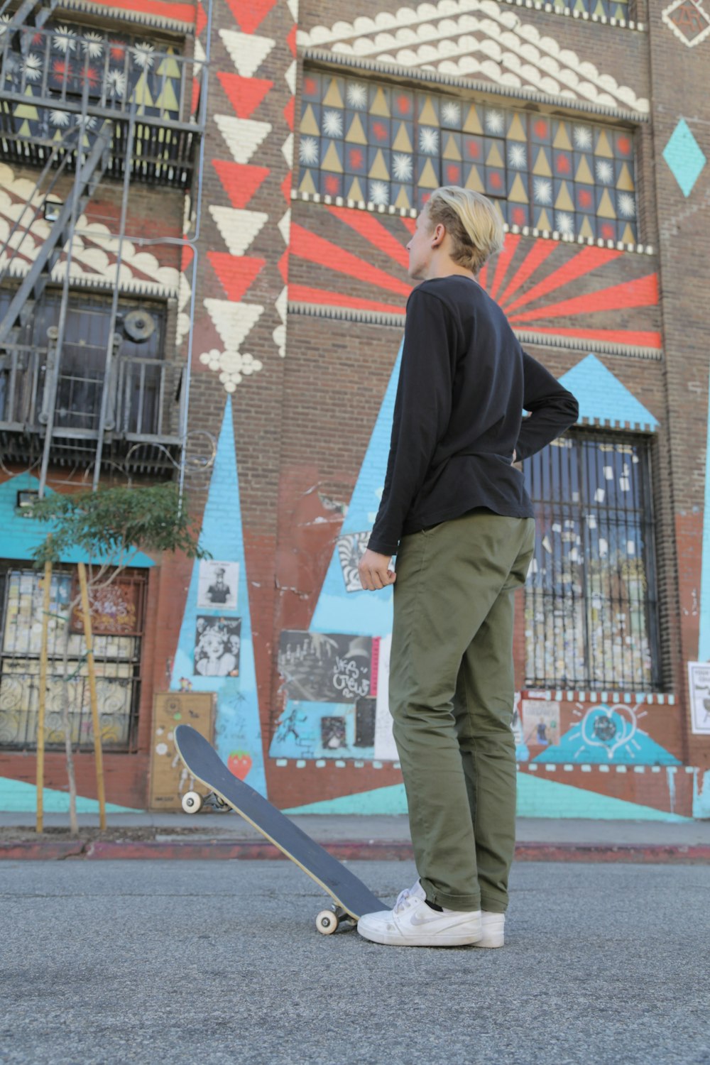 man in black long sleeve shirt and brown pants standing on brown wooden skateboard during daytime