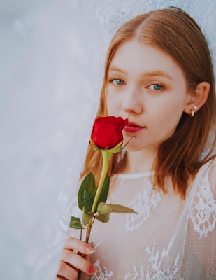 A model in a flowing rose-colored blouse smiling gently against a warm, golden-hued backdrop.