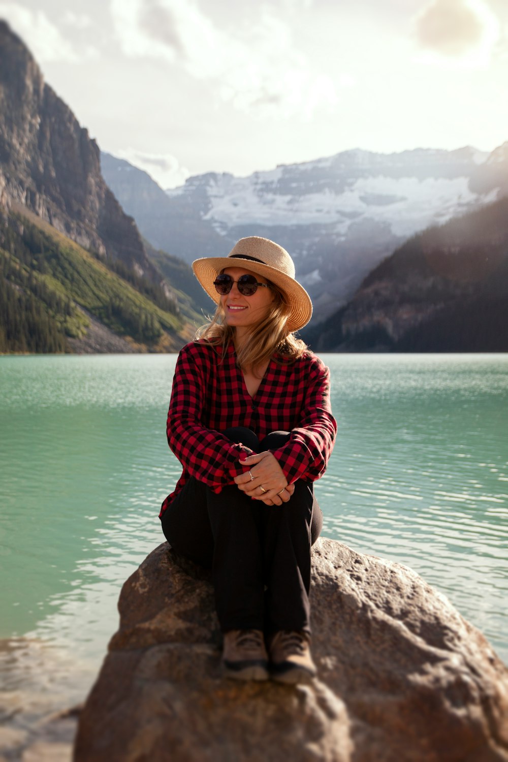 woman in red and white plaid dress shirt and black pants sitting on rock near body