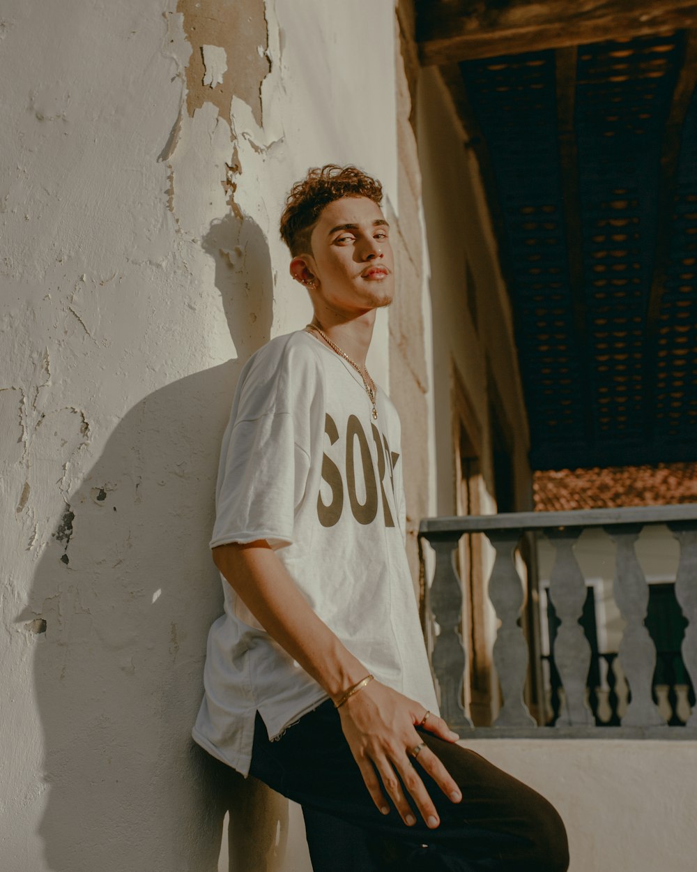 man in white crew neck t-shirt and black pants sitting on gray concrete fence during