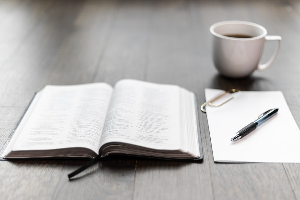 black pen on white book page beside white ceramic mug