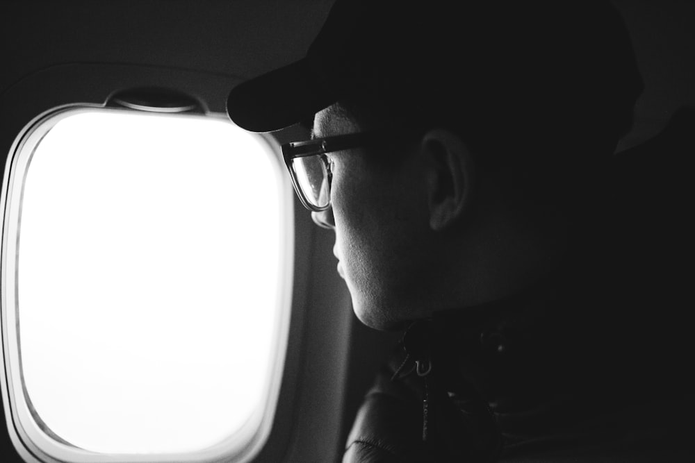 grayscale photo of man wearing black framed eyeglasses and black cap