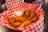 A basket filled with crispy fried chicken wings is placed on a table, lined with red and white checkered paper. A small, clear dipping sauce container with a creamy white sauce accompanies the chicken.