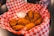 A basket filled with crispy fried chicken wings is placed on a table, lined with red and white checkered paper. A small, clear dipping sauce container with a creamy white sauce accompanies the chicken.