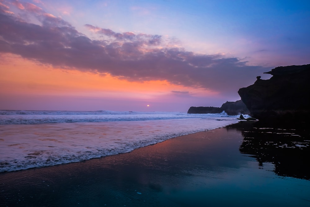 silhouette of person standing on seashore during sunset