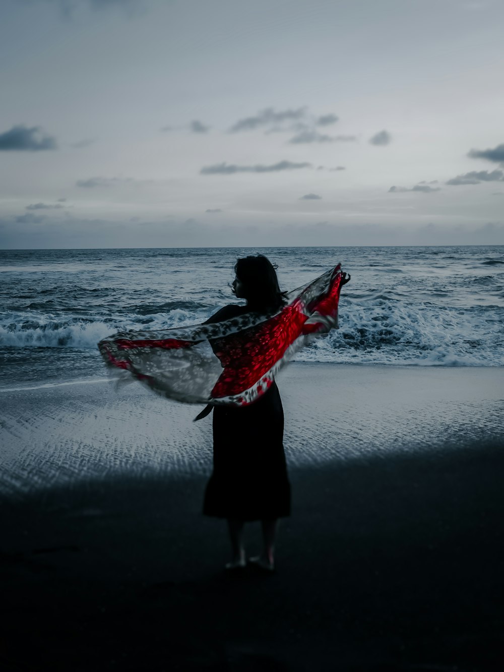 femme en robe noire tenant une planche de surf blanche et rouge sur la plage pendant la journée