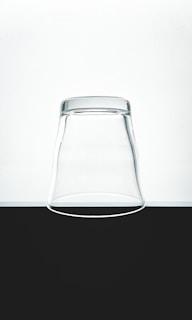An inverted clear glass placed on a flat surface, contrasting against a minimalistic black and white background.