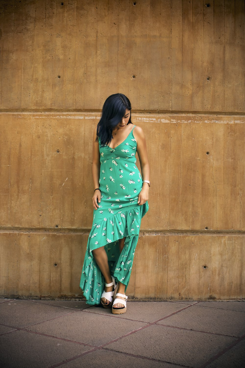 woman in green and white polka dot sleeveless dress standing beside brown wooden wall