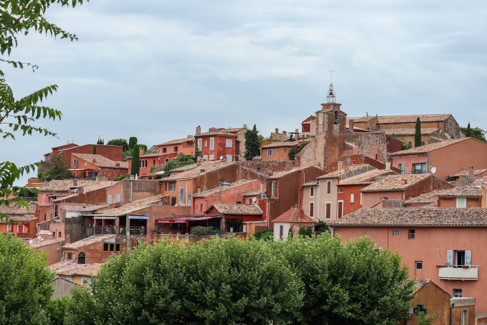 brown and white concrete houses near green trees under white clouds during daytime