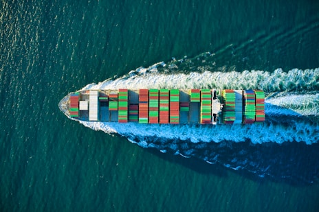 Close-up of a massive container ship cutting through deep blue ocean waters, representing vast logistics reach.