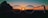 A pair of round glasses is held up against a backdrop of a sunset. The sun is positioned almost centrally within the lenses, creating a striking silhouette and casting warm hues across the frame.