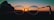 A pair of round glasses is held up against a backdrop of a sunset. The sun is positioned almost centrally within the lenses, creating a striking silhouette and casting warm hues across the frame.