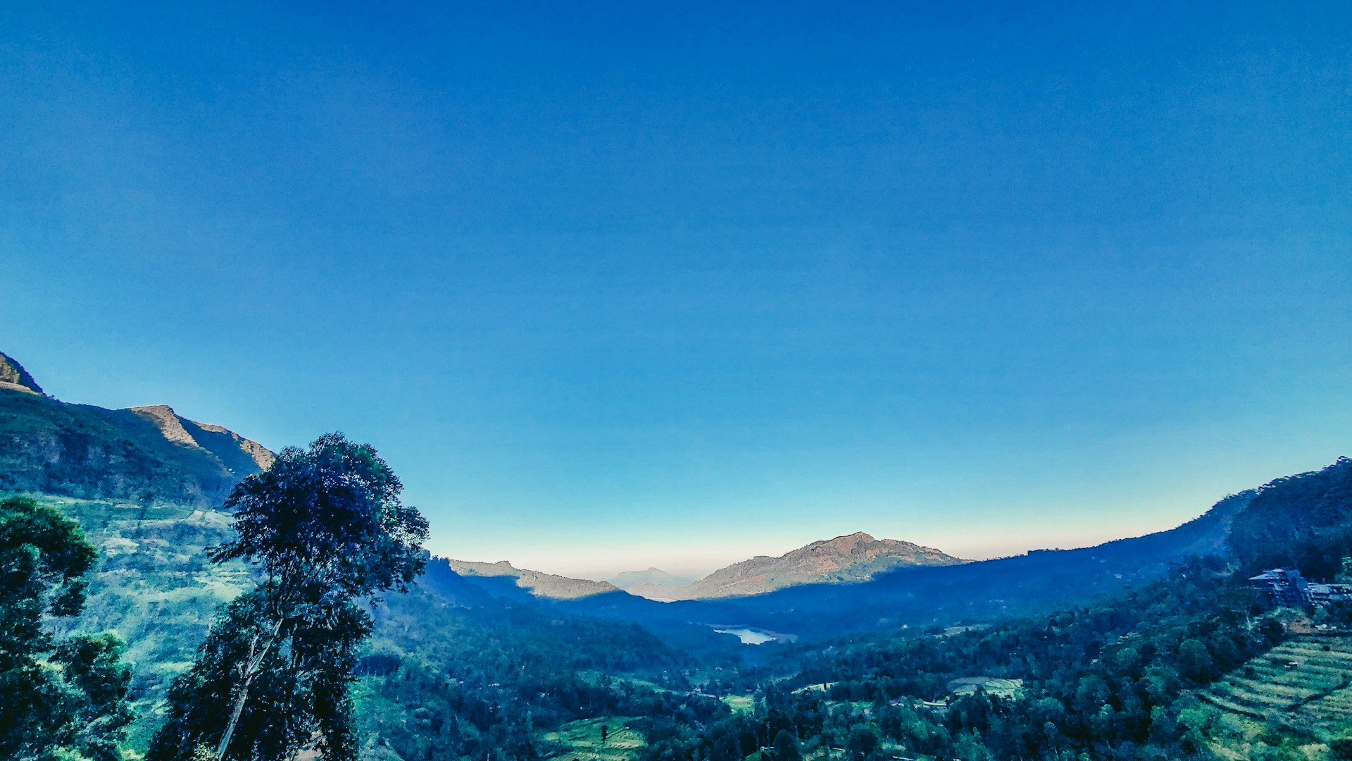 A breathtaking panoramic view of the lush green forests and rolling hills surrounding Villa Yacanto under a clear blue sky.