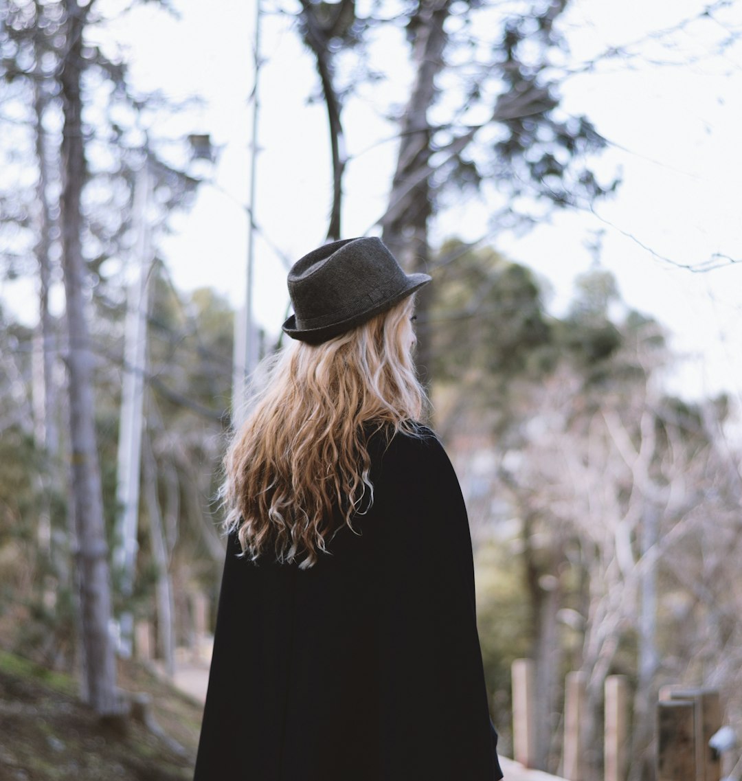 woman in black coat and black hat standing near trees during daytime