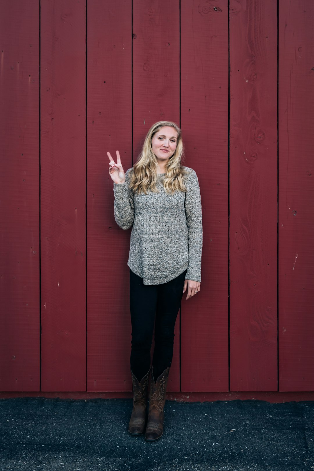 girl in gray and black long sleeve shirt standing beside red wooden wall