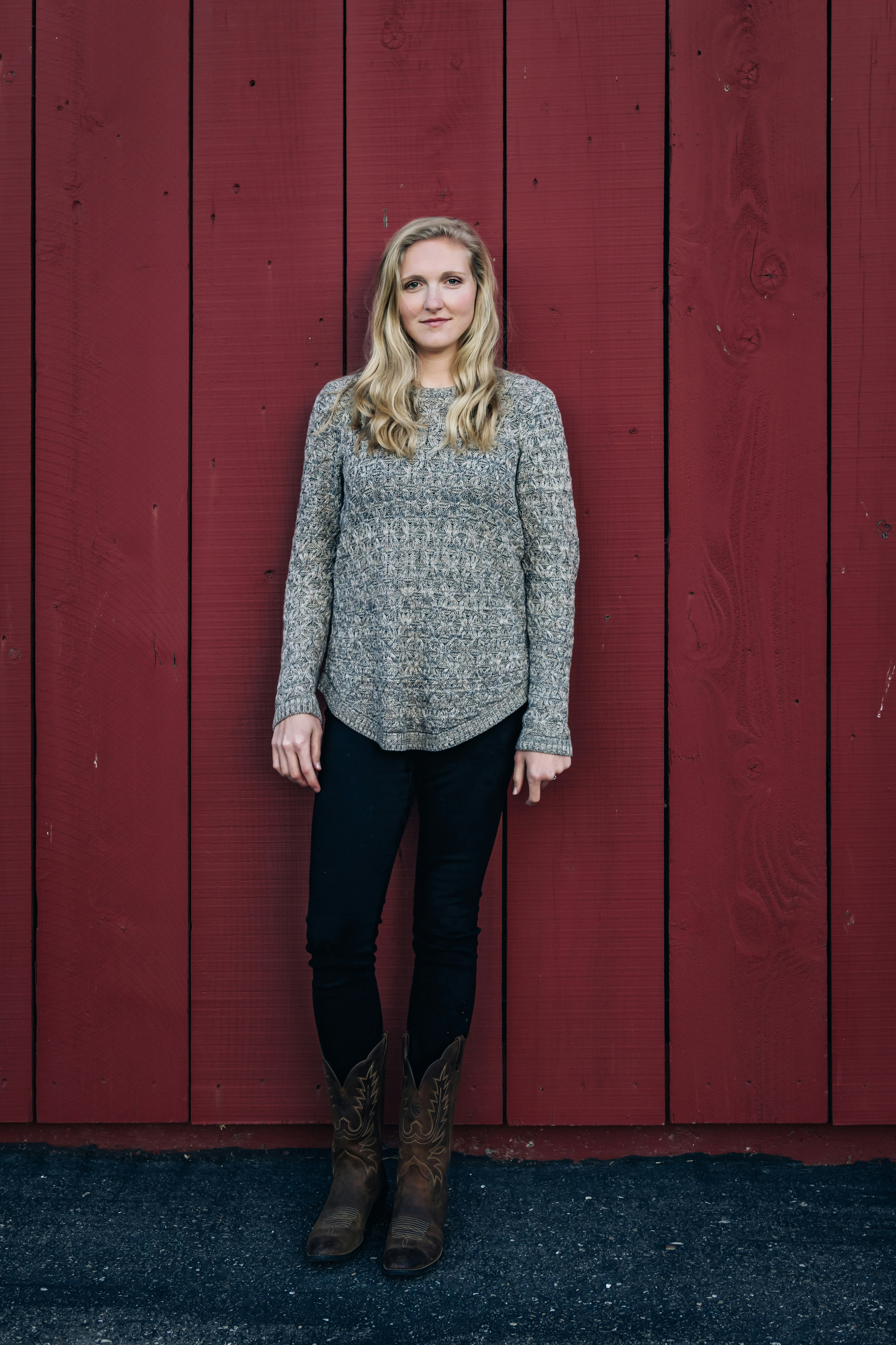 woman in gray sweater standing beside red wooden wall