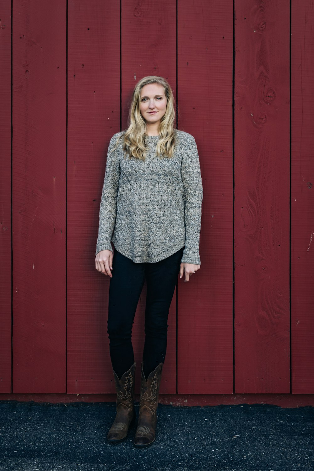 woman in gray sweater standing beside red wooden wall