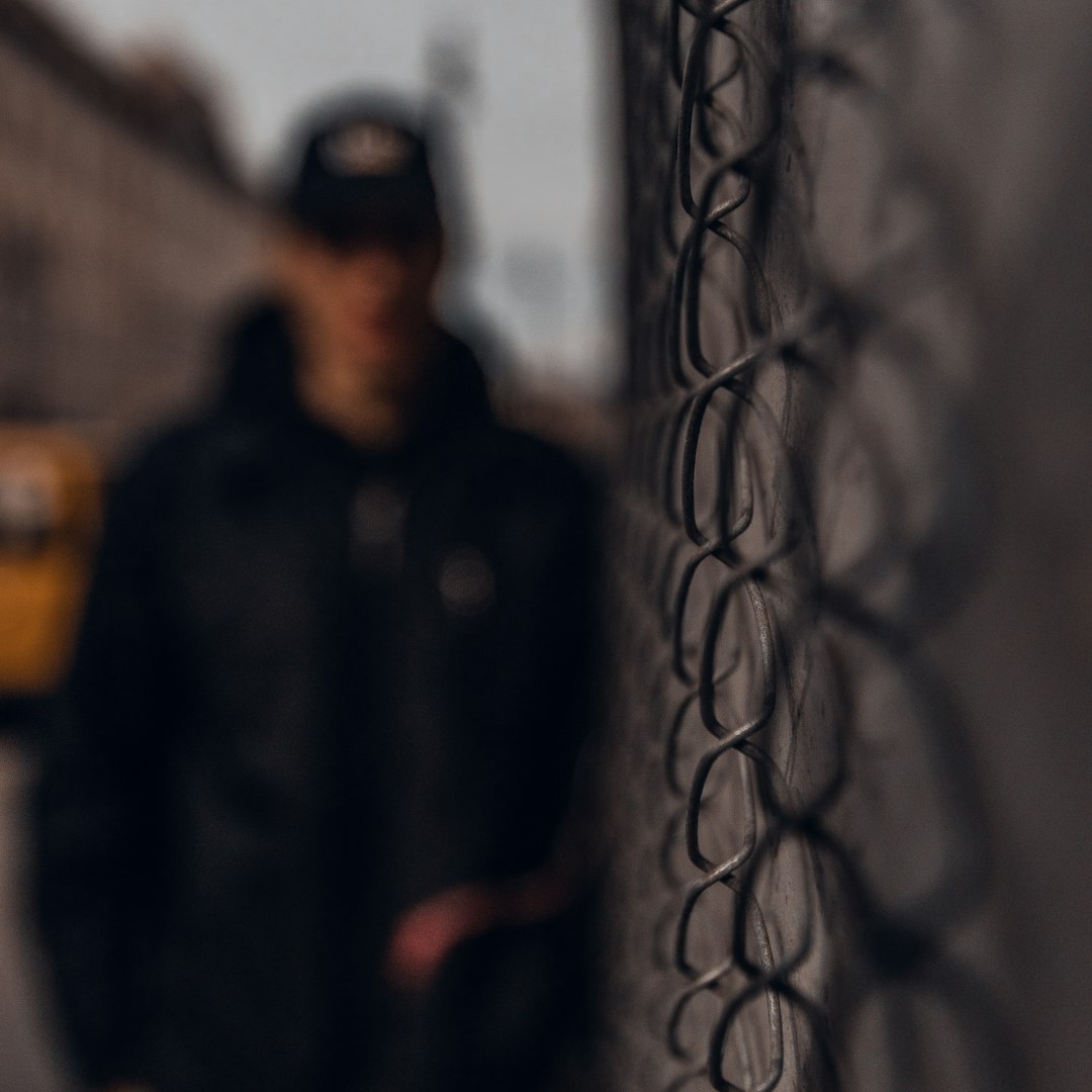 man in black jacket standing beside gray metal fence during daytime