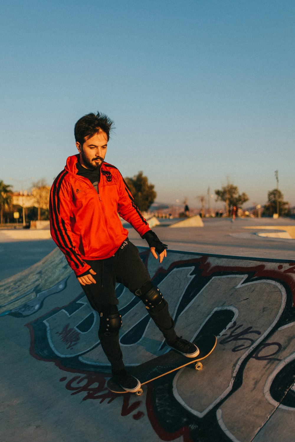 garçon en veste orange et pantalon noir debout sur le sol en béton gris pendant la journée