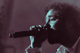 An artist singing into a microphone with expressive emotion in a warmly lit room.