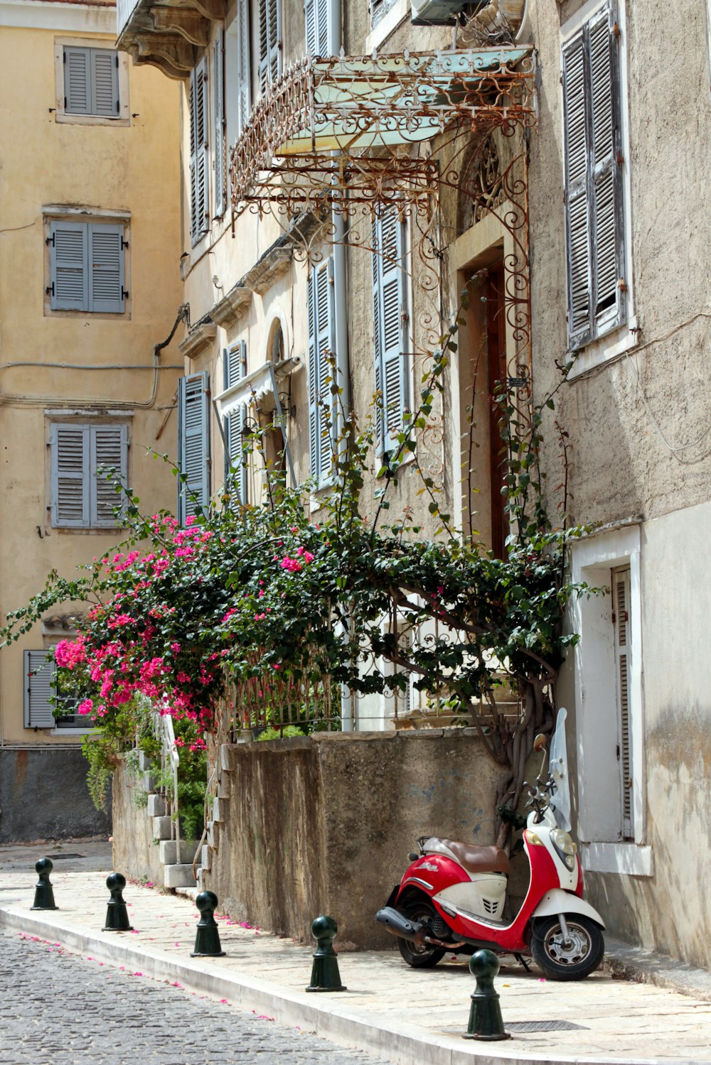 Motocicletta rossa parcheggiata accanto all'edificio in cemento bianco durante il giorno