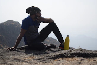 a man sitting on top of a mountain next to a yellow bottle