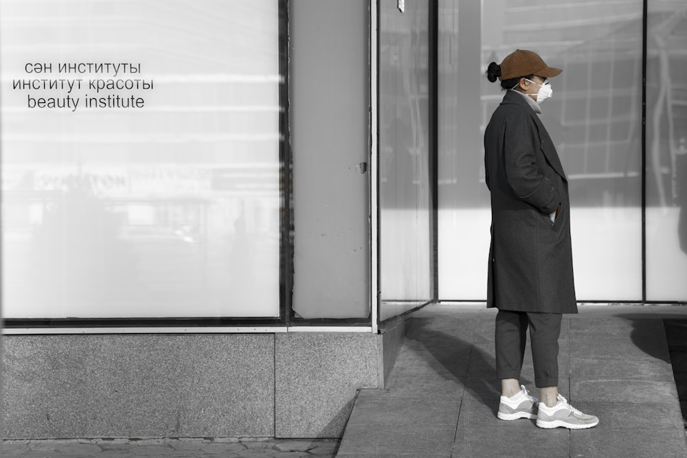 man in black coat and orange cap standing near white wall