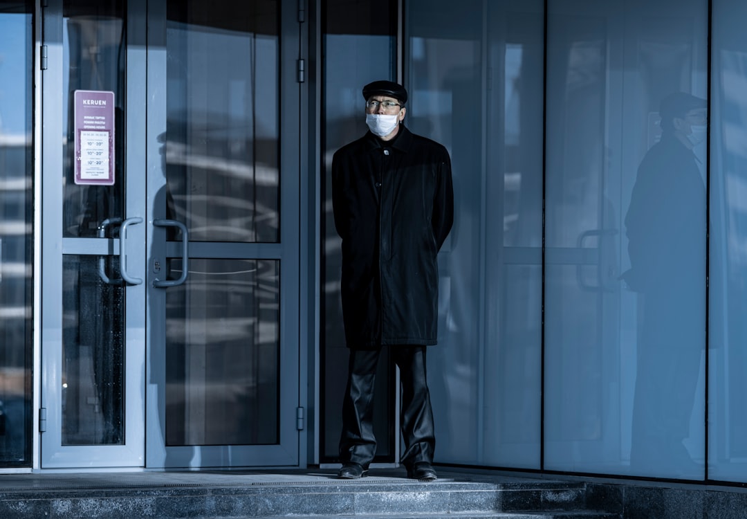man in black coat standing beside glass door