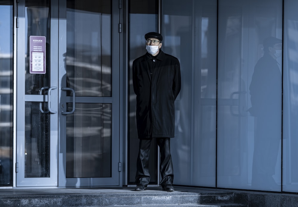 man in black coat standing beside glass door