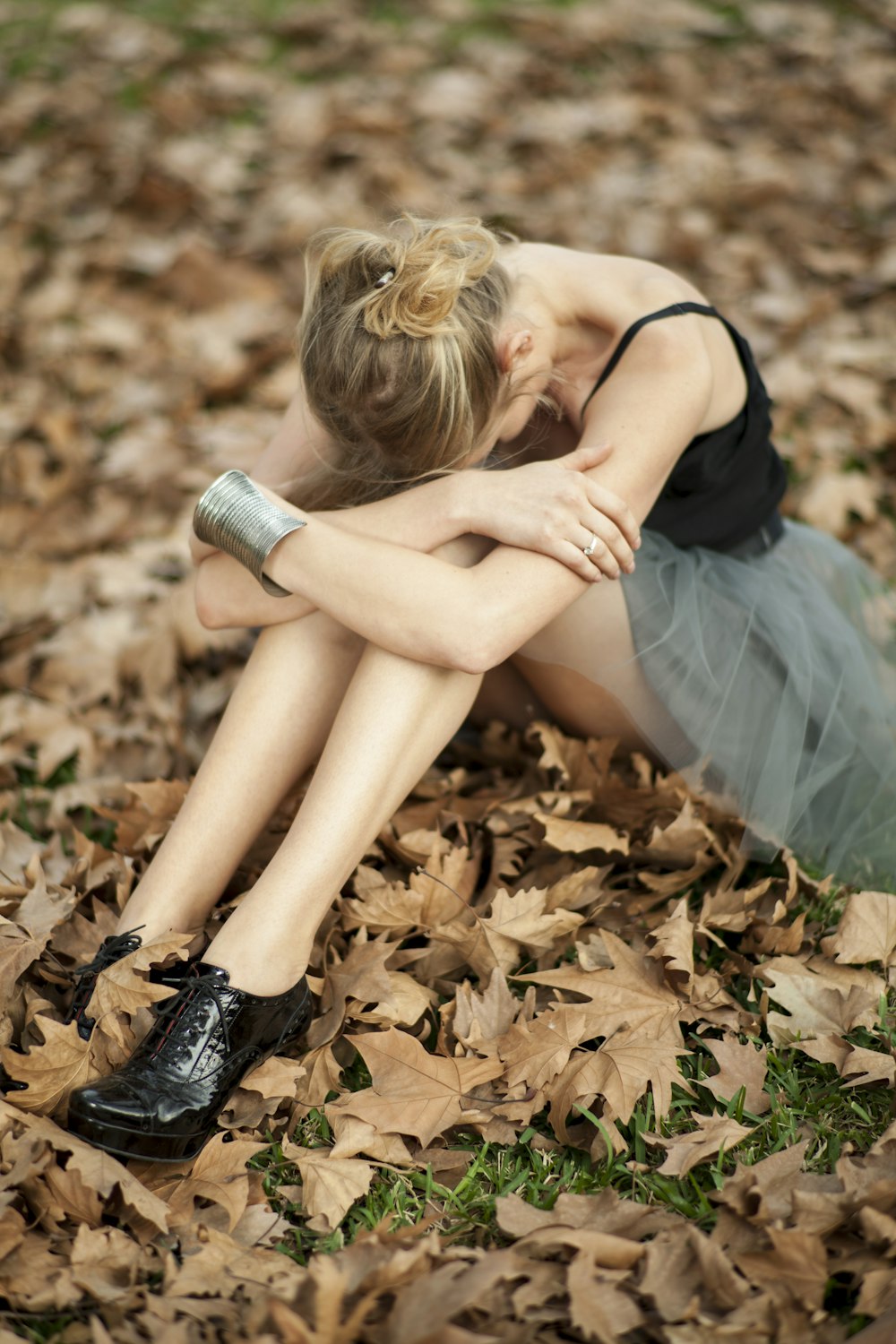 woman in black tank top and blue skirt sitting on dried leaves