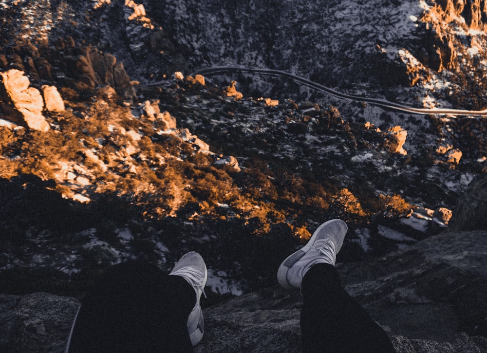 personne en pantalon noir et baskets blanches debout sur des feuilles séchées brunes