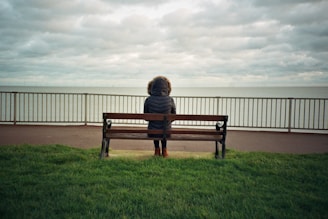 person sitting alone on brown wooden bench during daytime