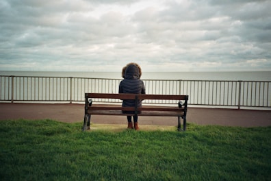 person sitting alone on brown wooden bench during daytime