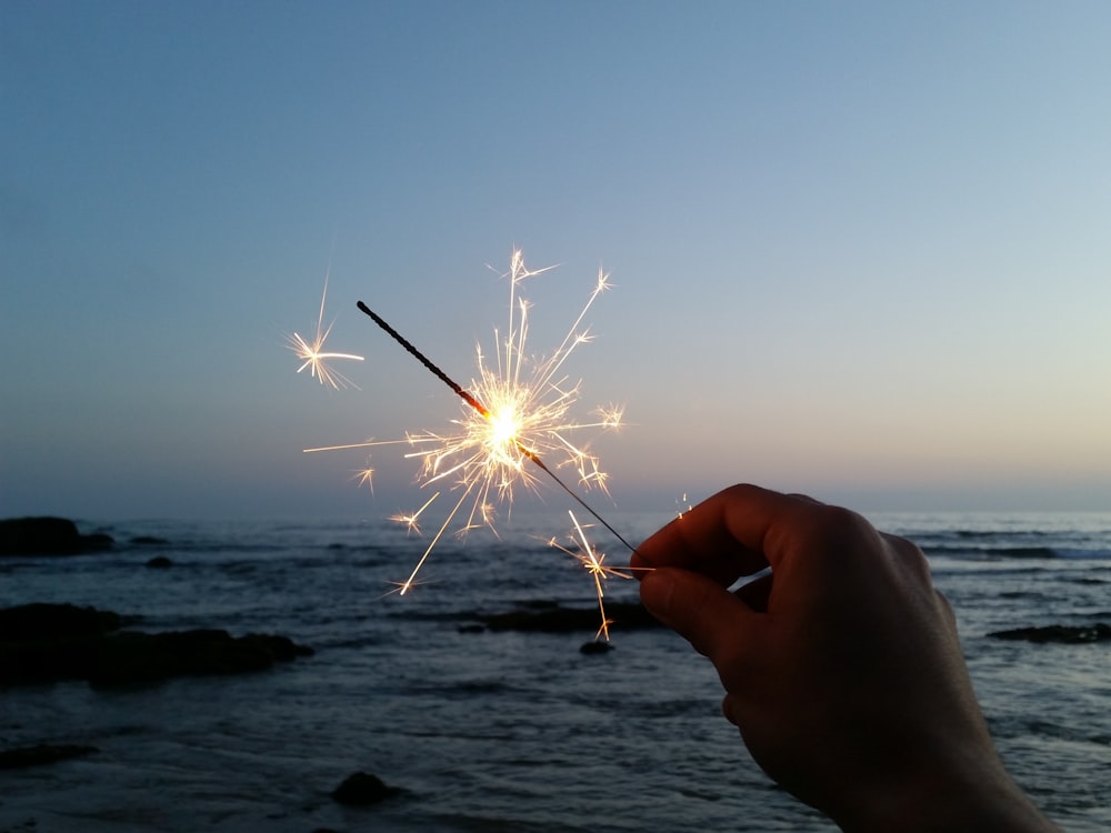 person holding sparkler in front of body of water during daytime