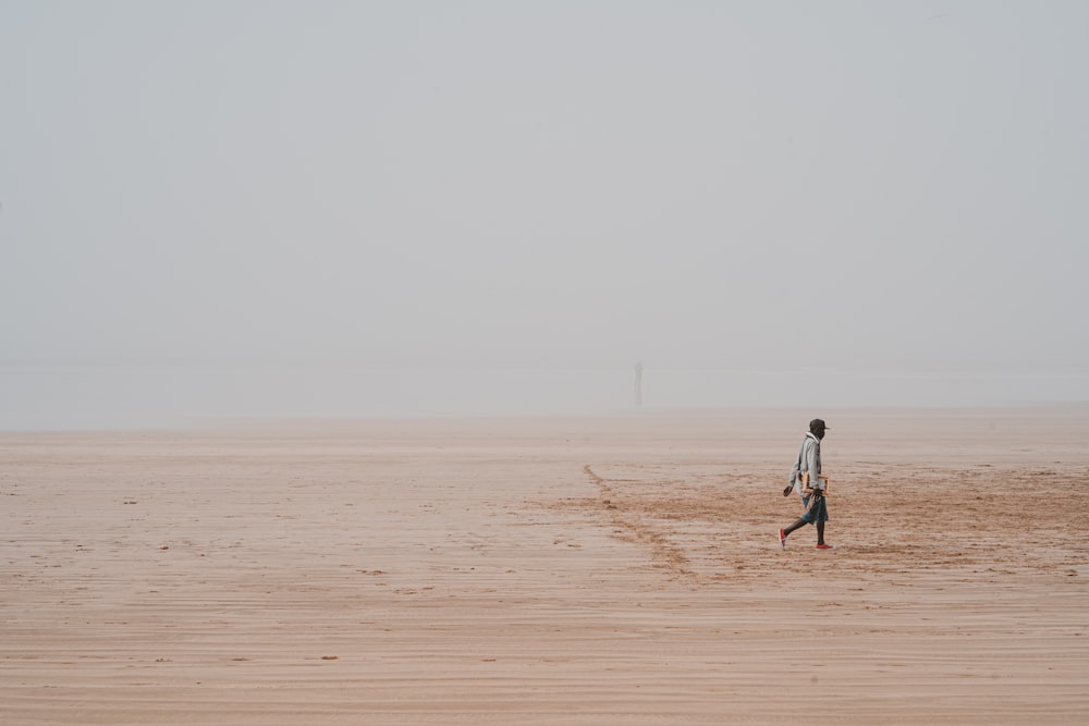 homme en chemise blanche marchant sur le sable brun pendant la journée