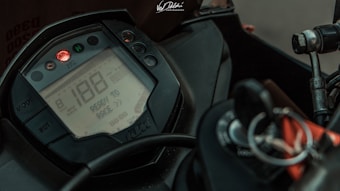 A close-up of a motorcycle dashboard featuring a digital display showing a speed of 188, with the phrase 'READY TO RACE'. The dashboard includes buttons marked 'MODE' and 'SET', along with a visible ignition switch and keychain. The color scheme is mostly black with a touch of red from the light indicators.