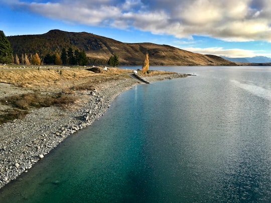 body of water near mountain under blue sky during daytime in Lake Tekapo Township New Zealand